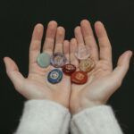Manos sosteniendo siete piedras de colores con símbolos grabados que representan los chakras del cuerpo humano.