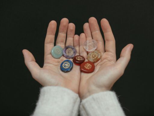 Manos sosteniendo siete piedras de colores con símbolos grabados que representan los chakras del cuerpo humano.