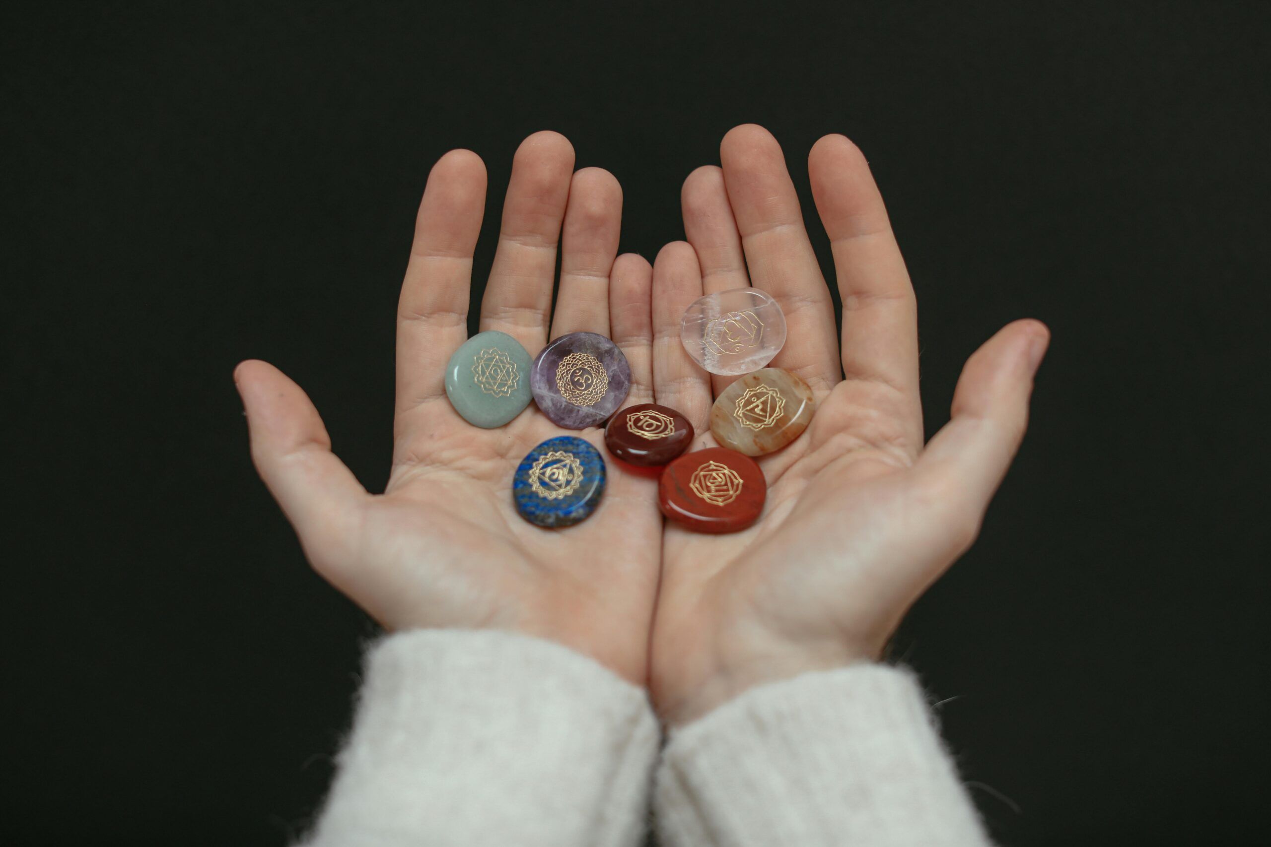Manos sosteniendo siete piedras de colores con símbolos grabados que representan los chakras del cuerpo humano.
