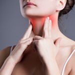 Mujer tocándose la zona tiroidea del cuello, destacada en rojo para representar síntomas relacionados con el hipertiroidismo.