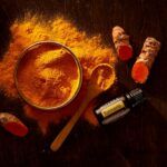 Cúrcuma en polvo con raíces frescas y frasco de extracto de curcumina sobre fondo oscuro, utilizada como antiinflamatorio natural para el dolor articular.