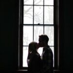 Pareja besándose frente a una ventana, simbolizando la influencia del pasado emocional en las relaciones de pareja.