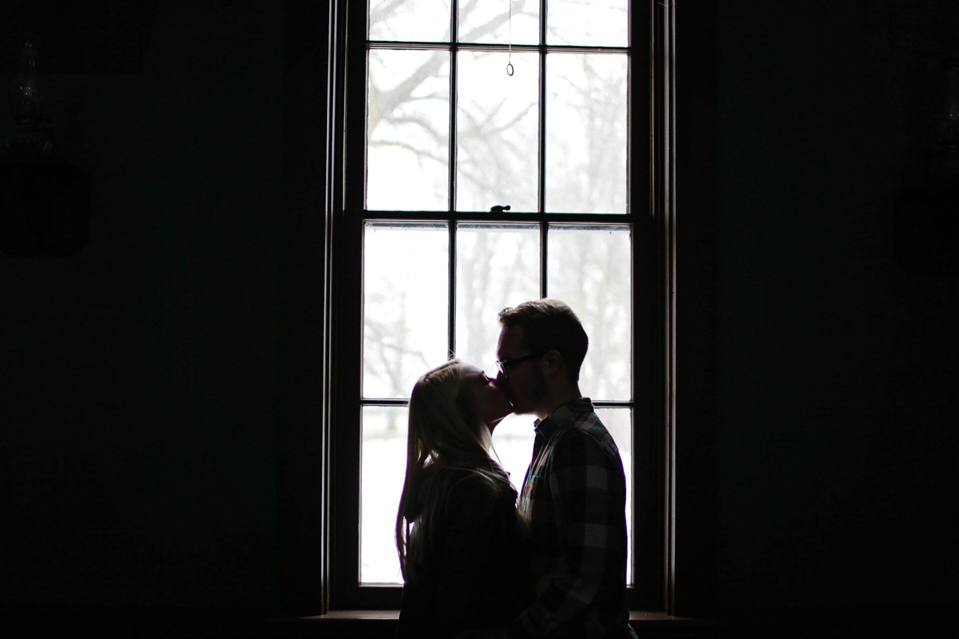 Pareja besándose frente a una ventana, simbolizando la influencia del pasado emocional en las relaciones de pareja.