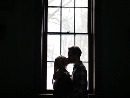 Pareja besándose frente a una ventana, simbolizando la influencia del pasado emocional en las relaciones de pareja.