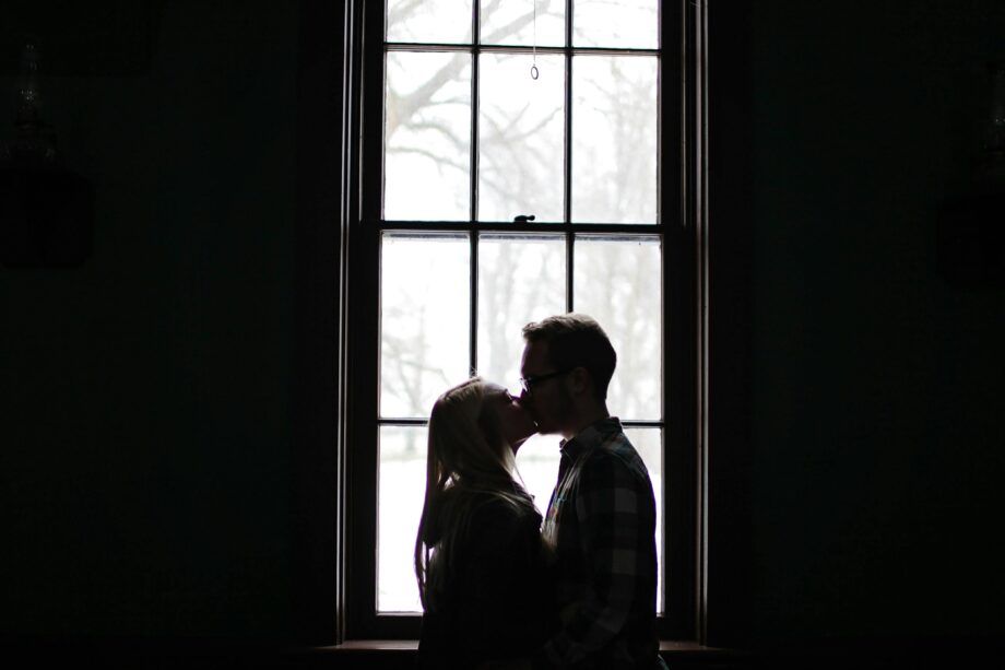 Pareja besándose frente a una ventana, simbolizando la influencia del pasado emocional en las relaciones de pareja.