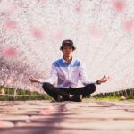 Hombre meditando en posición de loto bajo árboles en flor, simbolizando calma, equilibrio interior y el poder de los mantras para transformar la vida.