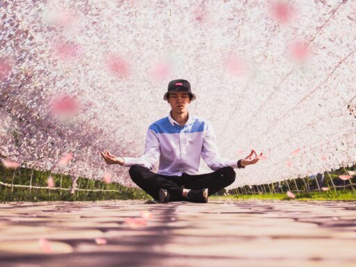 Hombre meditando en posición de loto bajo árboles en flor, simbolizando calma, equilibrio interior y el poder de los mantras para transformar la vida.
