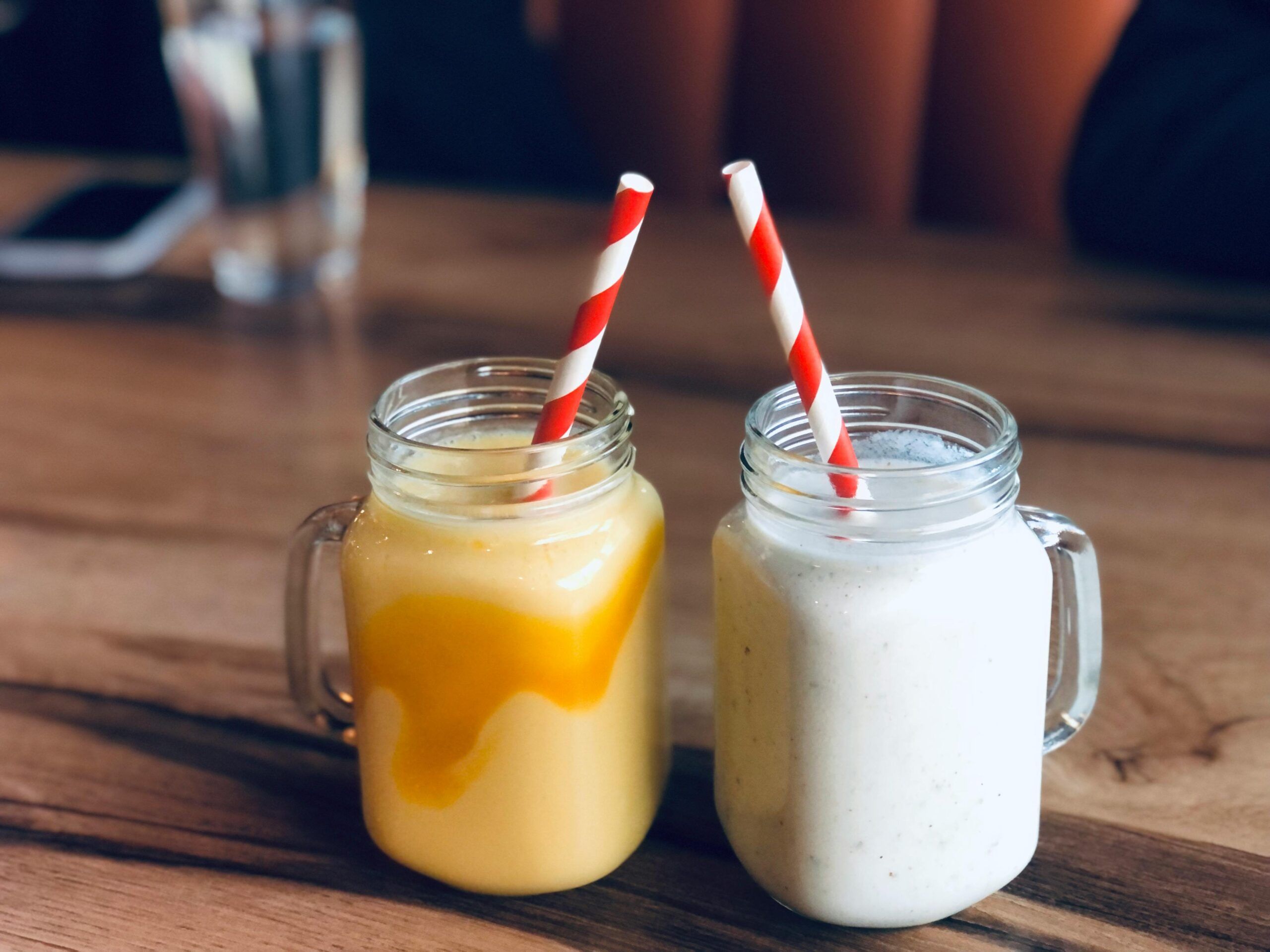 Dos batidos en frascos de vidrio con pajillas, uno de color mango y otro cremoso, que aparentan ser saludables pero pueden contener altos niveles de azúcar.