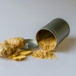 Raíz de jengibre fresco con rodajas y jengibre en polvo derramado de un recipiente, especia natural con propiedades antiinflamatorias.