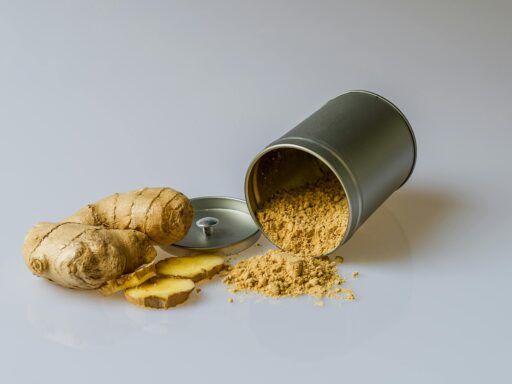 Raíz de jengibre fresco con rodajas y jengibre en polvo derramado de un recipiente, especia natural con propiedades antiinflamatorias.