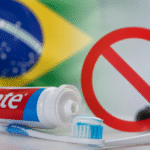 Pasta dental Colgate con cepillo de dientes y bandera de Brasil al fondo, simbolizando la polémica sobre su posible prohibición.