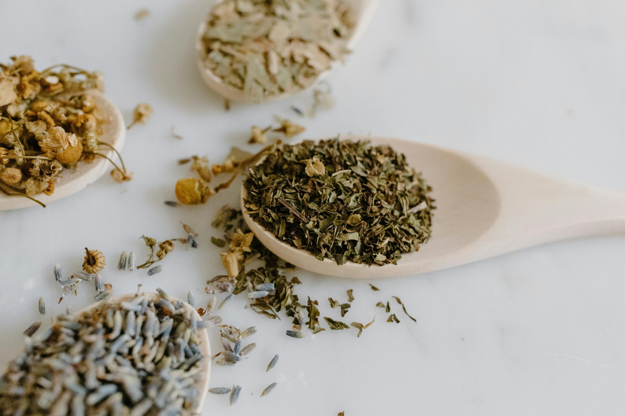 Primer plano de cucharas de madera con manzanilla, lavanda y otras hierbas secas usadas para infusiones relajantes contra la ansiedad.