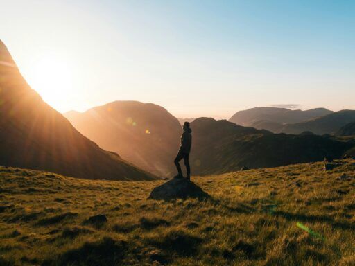 Persona de pie sobre una roca en medio de un valle montañoso al amanecer, simbolizando la conexión con la naturaleza.
