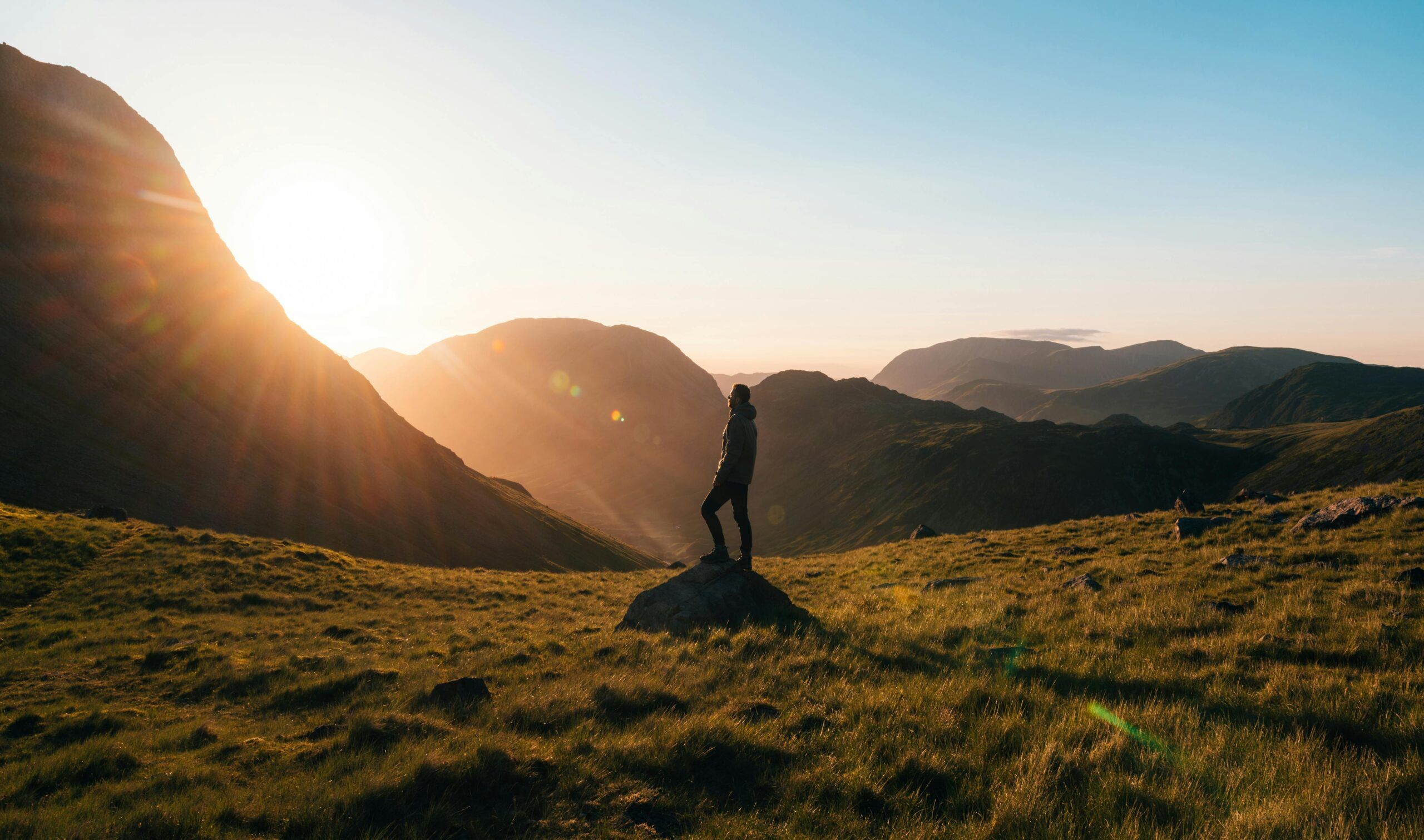 Persona de pie sobre una roca en medio de un valle montañoso al amanecer, simbolizando la conexión con la naturaleza.