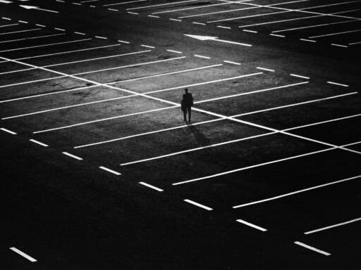 Figura solitaria de un hombre en un gran estacionamiento vacío iluminado en contraste, representando sentimientos de abandono y soledad emocional.
