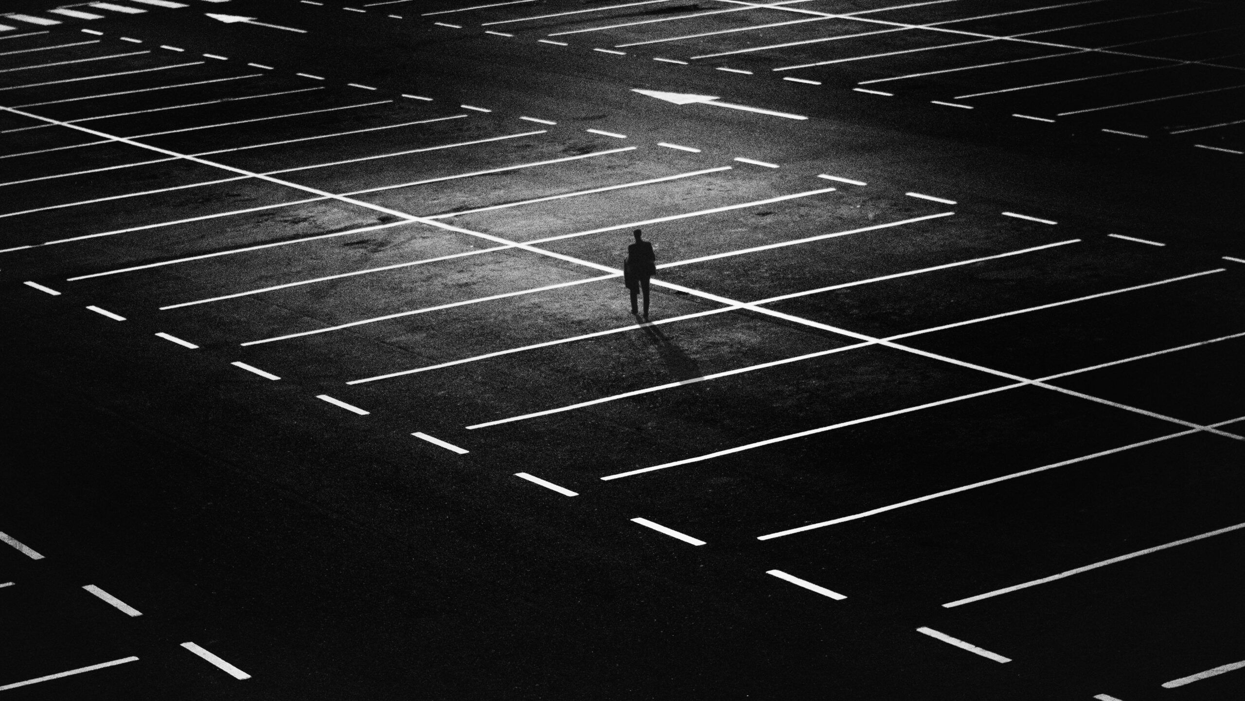 Figura solitaria de un hombre en un gran estacionamiento vacío iluminado en contraste, representando sentimientos de abandono y soledad emocional.