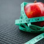 Manzana roja envuelta con una cinta métrica sobre una superficie oscura, representando el metabolismo y el control del peso.