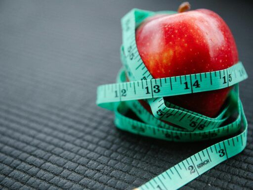 Manzana roja envuelta con una cinta métrica sobre una superficie oscura, representando el metabolismo y el control del peso.