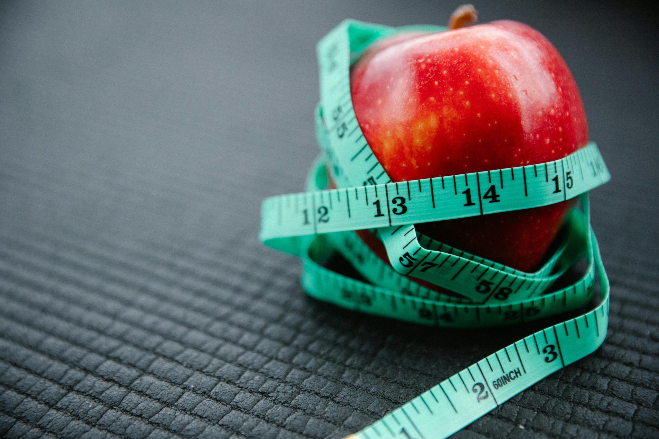 Manzana roja envuelta con una cinta métrica sobre una superficie oscura, representando el metabolismo y el control del peso.