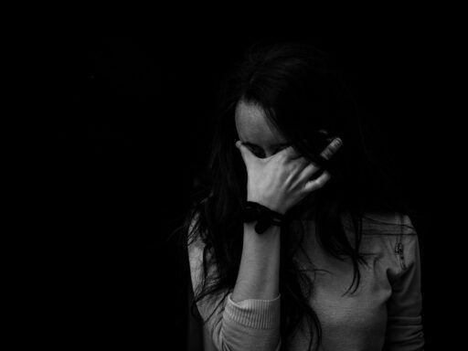 Persona cubriéndose el rostro con la mano en un gesto de tristeza, representando el peso de las heridas emocionales que pueden abordarse con constelaciones familiares.