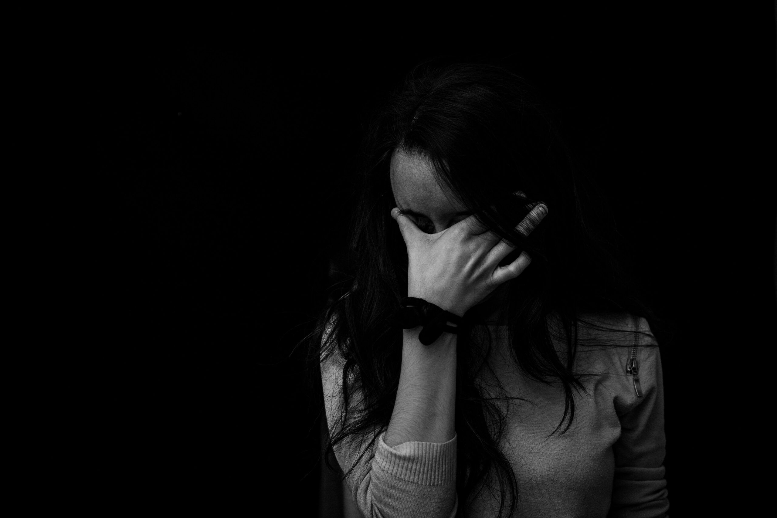 Persona cubriéndose el rostro con la mano en un gesto de tristeza, representando el peso de las heridas emocionales que pueden abordarse con constelaciones familiares.