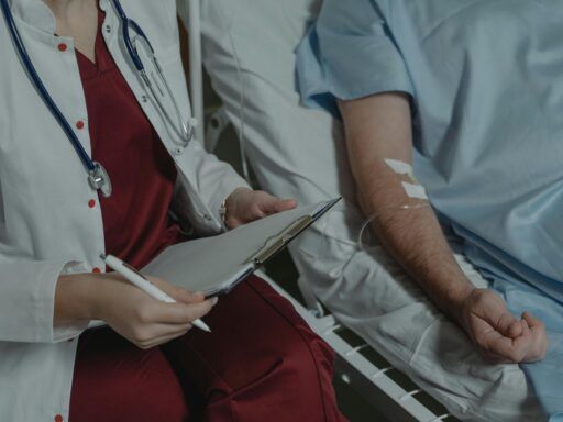 Profesional médico tomando notas junto a un paciente hospitalizado con una vía intravenosa en el brazo.