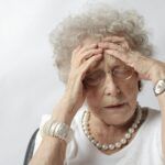 Mujer adulta mayor con expresión de dolor o confusión tocándose la cabeza, ilustrando síntomas cognitivos relacionados con el Alzheimer.