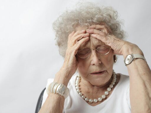 Mujer adulta mayor con expresión de dolor o confusión tocándose la cabeza, ilustrando síntomas cognitivos relacionados con el Alzheimer.