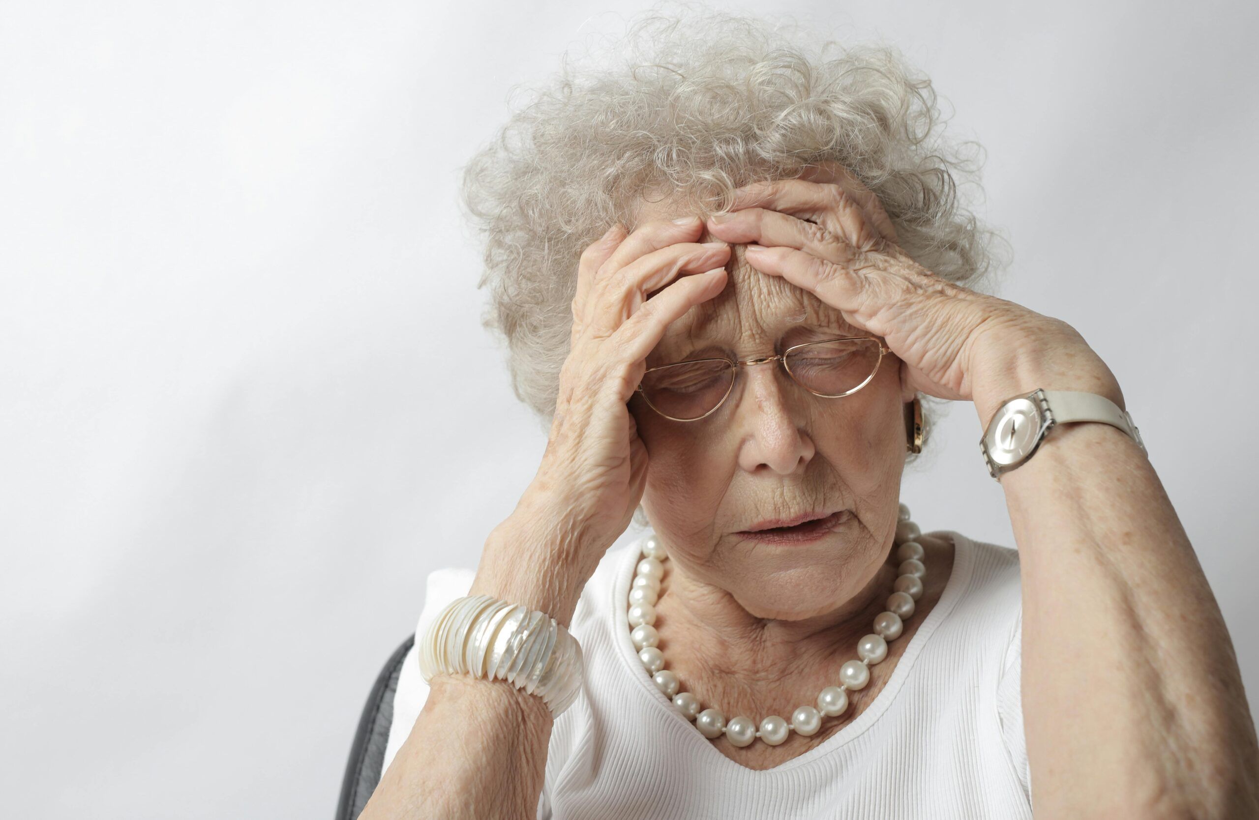 Mujer adulta mayor con expresión de dolor o confusión tocándose la cabeza, ilustrando síntomas cognitivos relacionados con el Alzheimer.