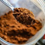 Cucharada de proteína en polvo dentro de un envase, utilizada como suplemento alimenticio, asociada a posibles riesgos por contaminación con plomo.