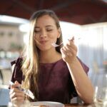 Mujer comiendo con cubiertos metálicos, ejemplo del contacto entre utensilios de cocina y alimentos que puede provocar migración de metales.