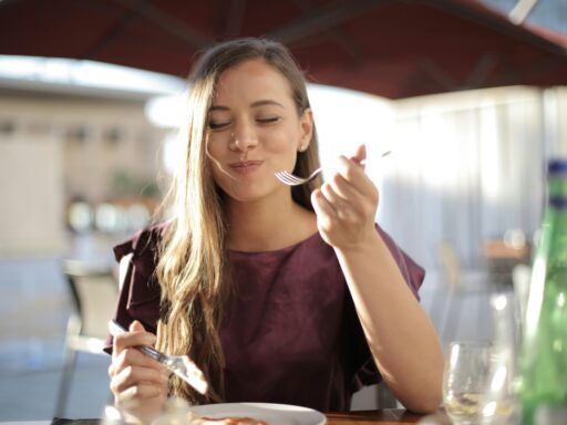 Mujer comiendo con cubiertos metálicos, ejemplo del contacto entre utensilios de cocina y alimentos que puede provocar migración de metales.
