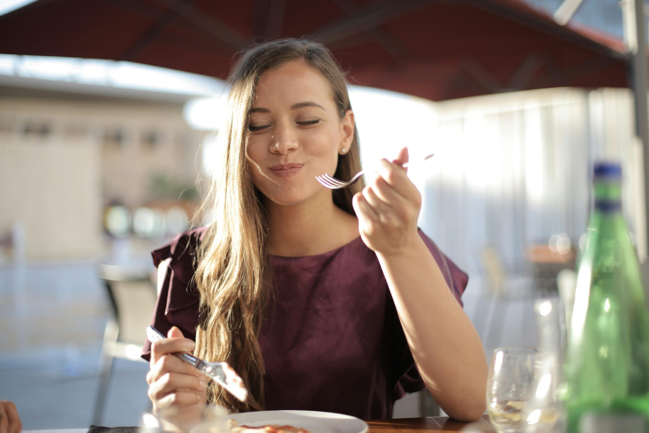 Mujer comiendo con cubiertos metálicos, ejemplo del contacto entre utensilios de cocina y alimentos que puede provocar migración de metales.