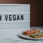 Cartel con la palabra “VEGAN” junto a un plato de comida vegana con tostadas, tomate y aguacate.