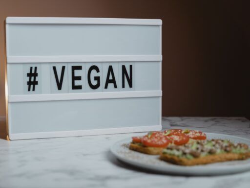 Cartel con la palabra “VEGAN” junto a un plato de comida vegana con tostadas, tomate y aguacate.