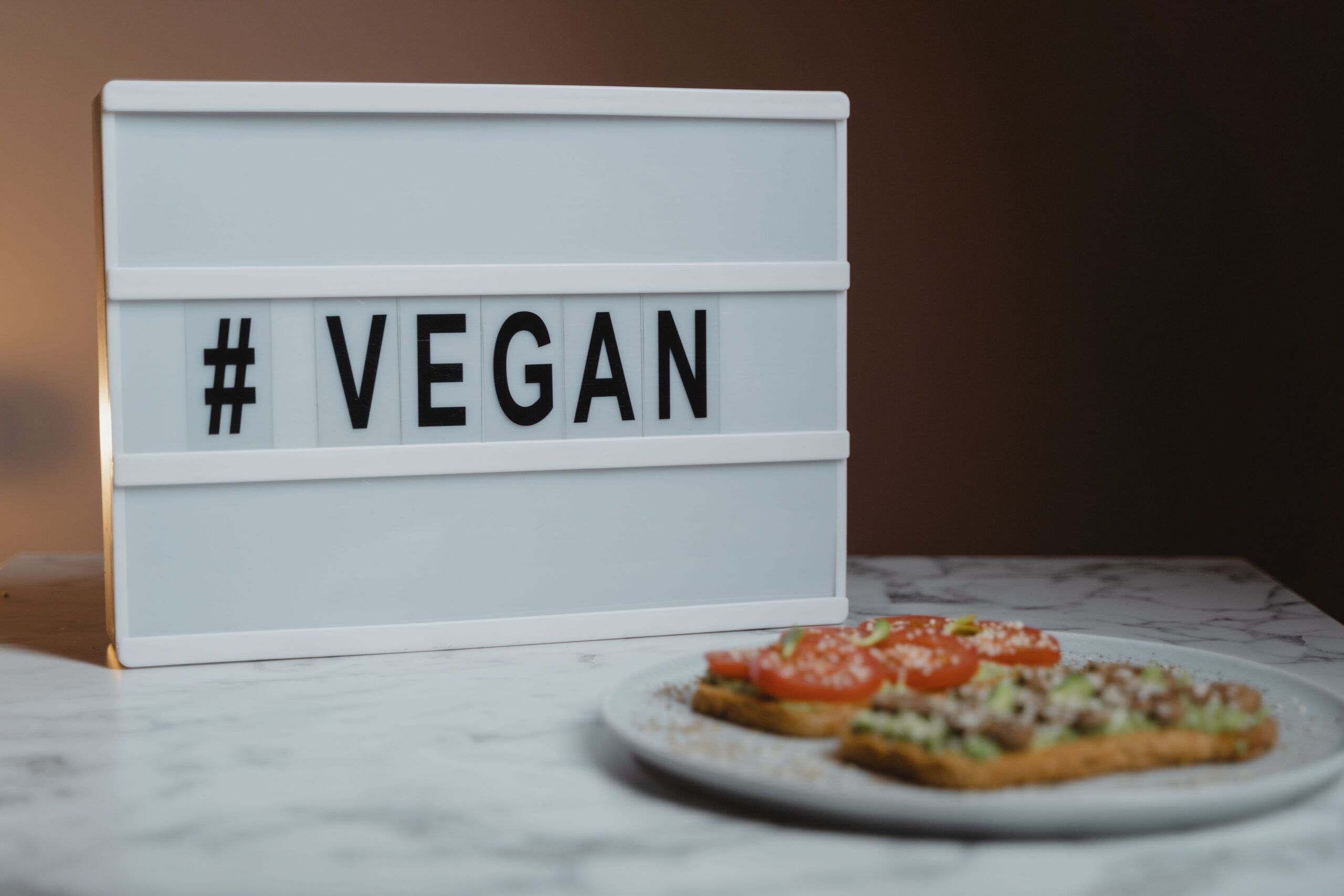 Cartel con la palabra “VEGAN” junto a un plato de comida vegana con tostadas, tomate y aguacate.