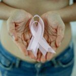 Manos sosteniendo un lazo rosa en apoyo a la concienciación sobre el cáncer de mama en mujeres jóvenes.