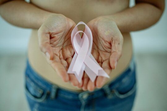 Manos sosteniendo un lazo rosa en apoyo a la concienciación sobre el cáncer de mama en mujeres jóvenes.