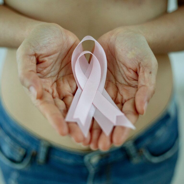 Manos sosteniendo un lazo rosa en apoyo a la concienciación sobre el cáncer de mama en mujeres jóvenes.